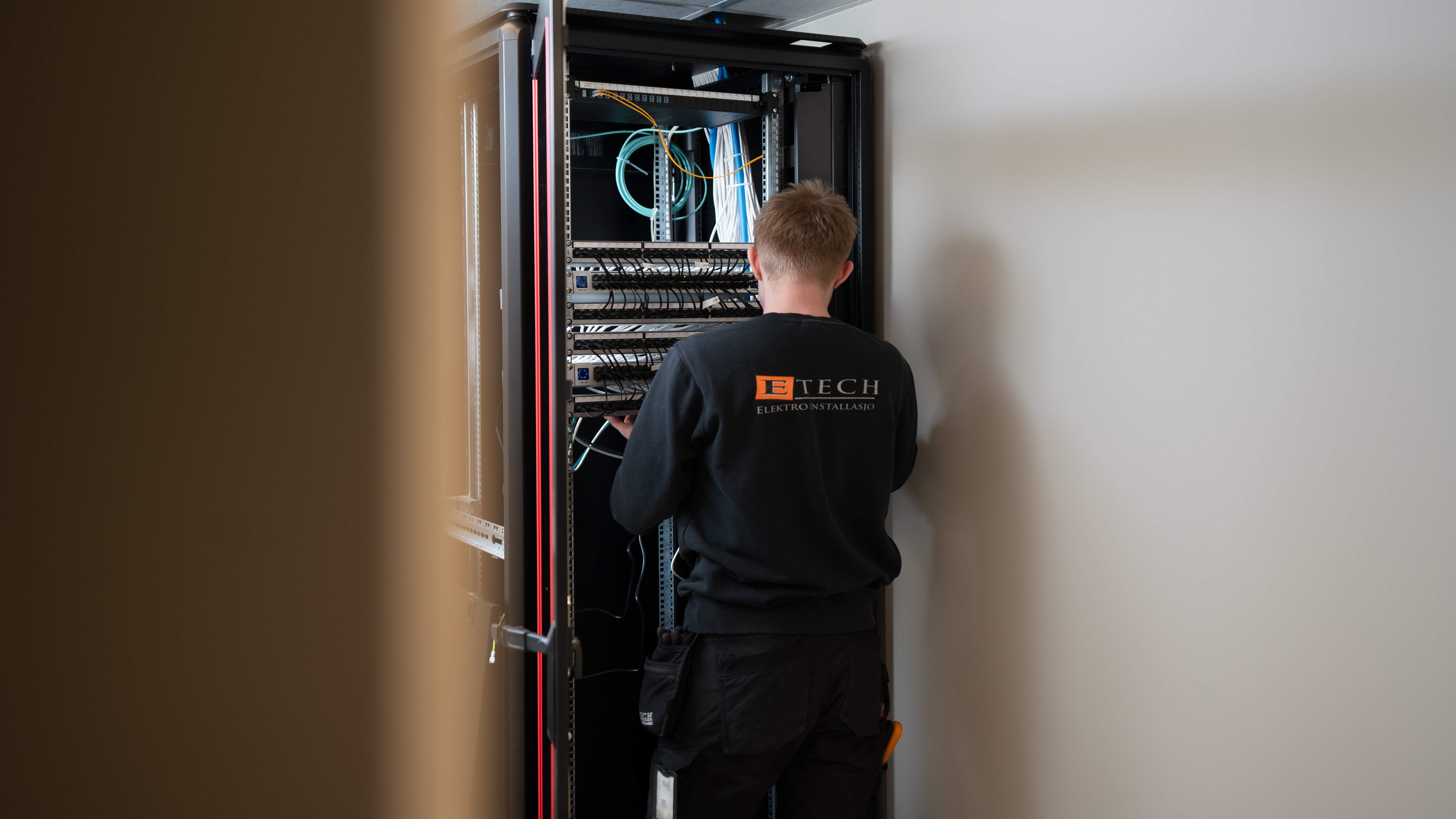 Elektriker fra E-Tech kobler nettverksrack med patchekabler i et næringsbygg